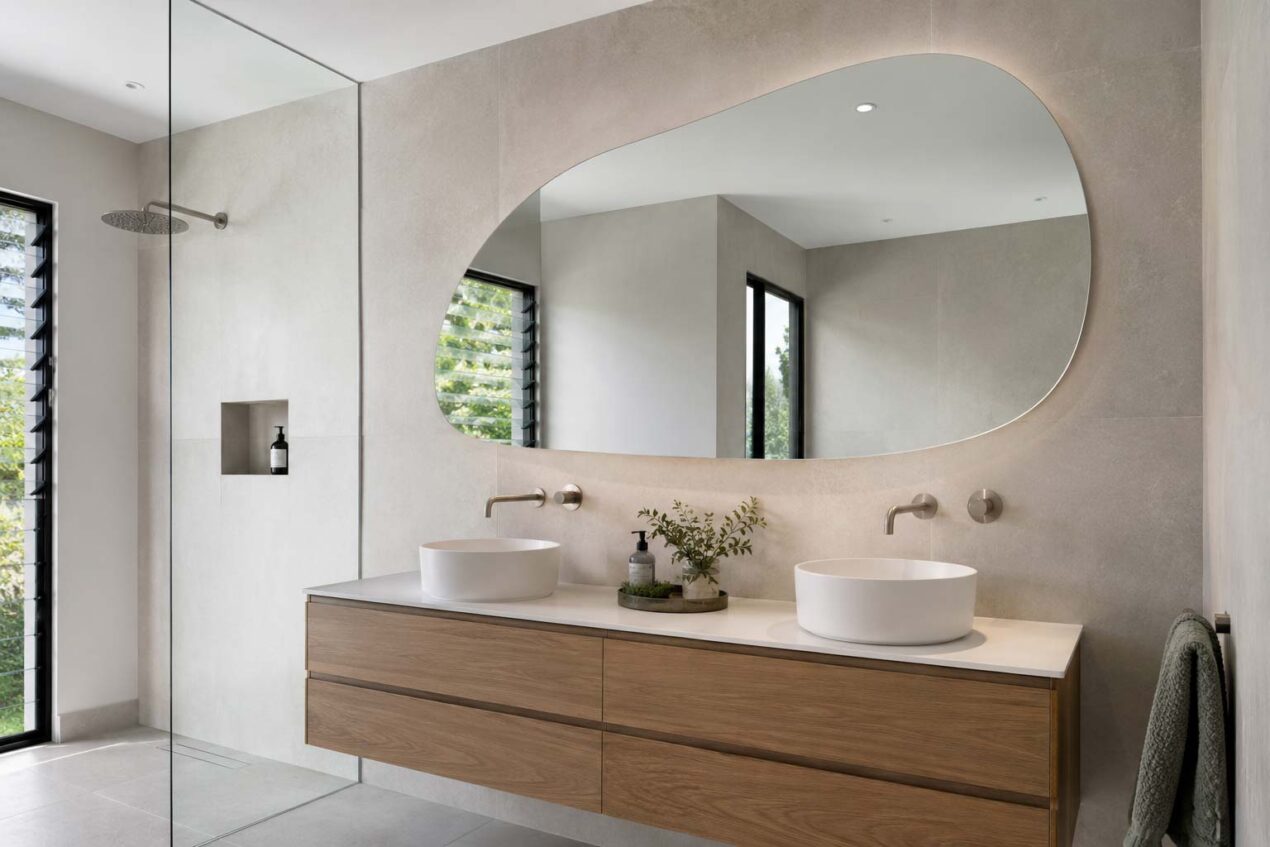 Modern bathroom vanity with an organic shaped frameless mirror reflecting natural light
