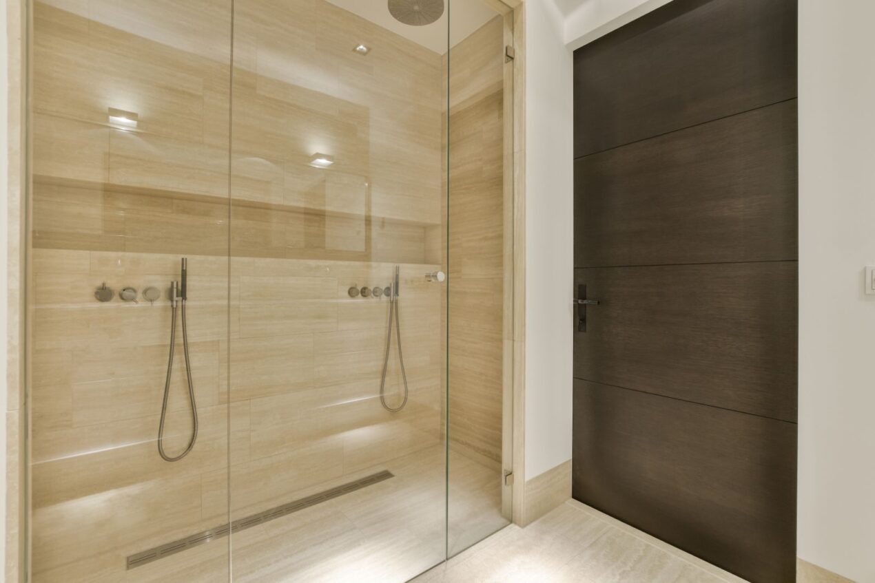 A luxury bathroom with a wall-to-wall glass screen and double shower, styled in warm natural tones