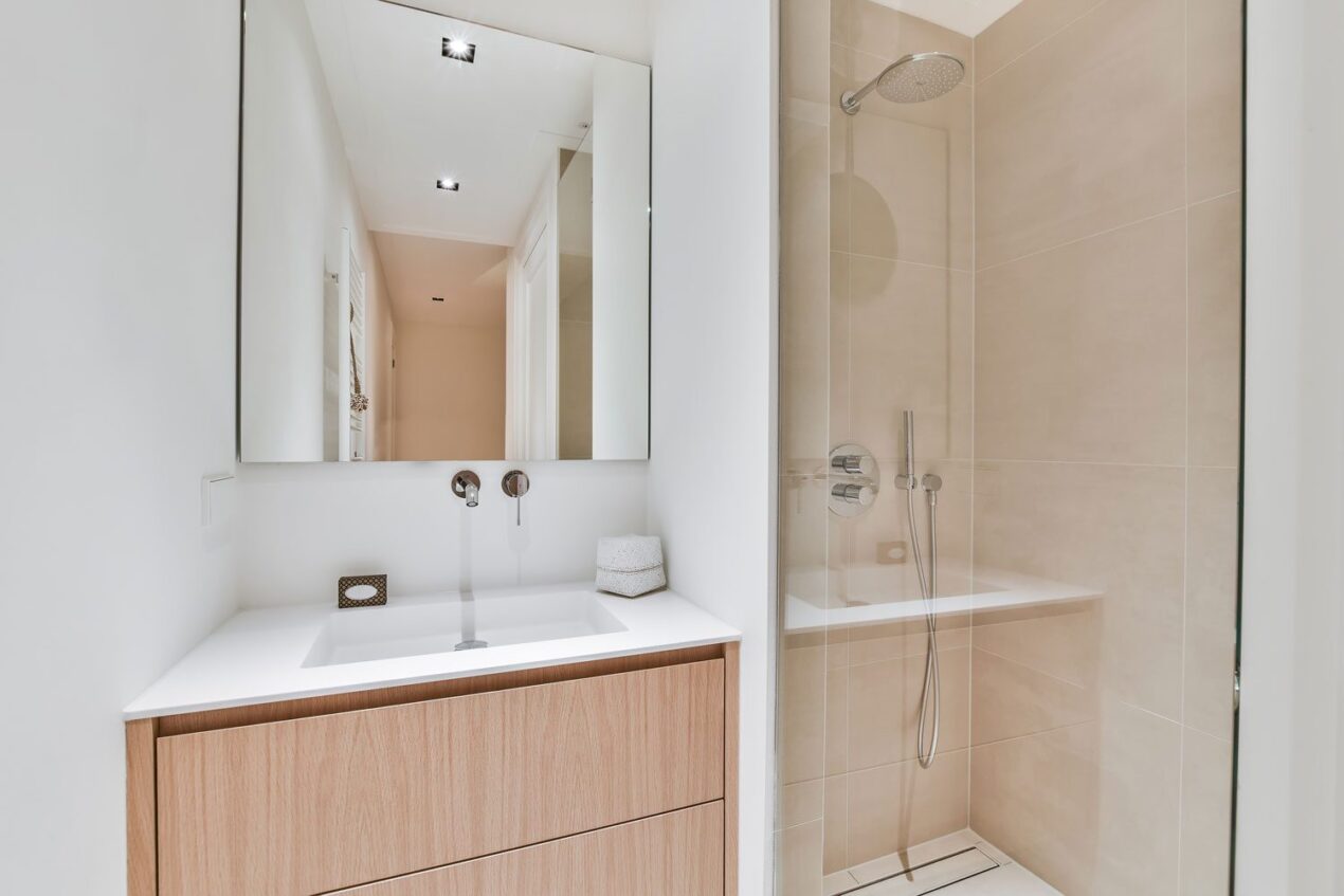 Stylish frameless shower doors next to a light wood vanity in a minimalist ensuite