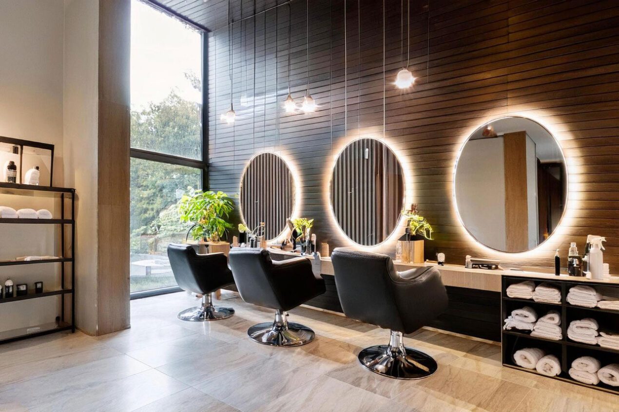 Modern salon interior with backlit round mirrors and black hairdressing chairs in front of a timber feature wall