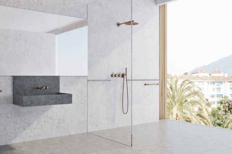 Frameless shower glass panel in a light grey bathroom with brushed gold fittings