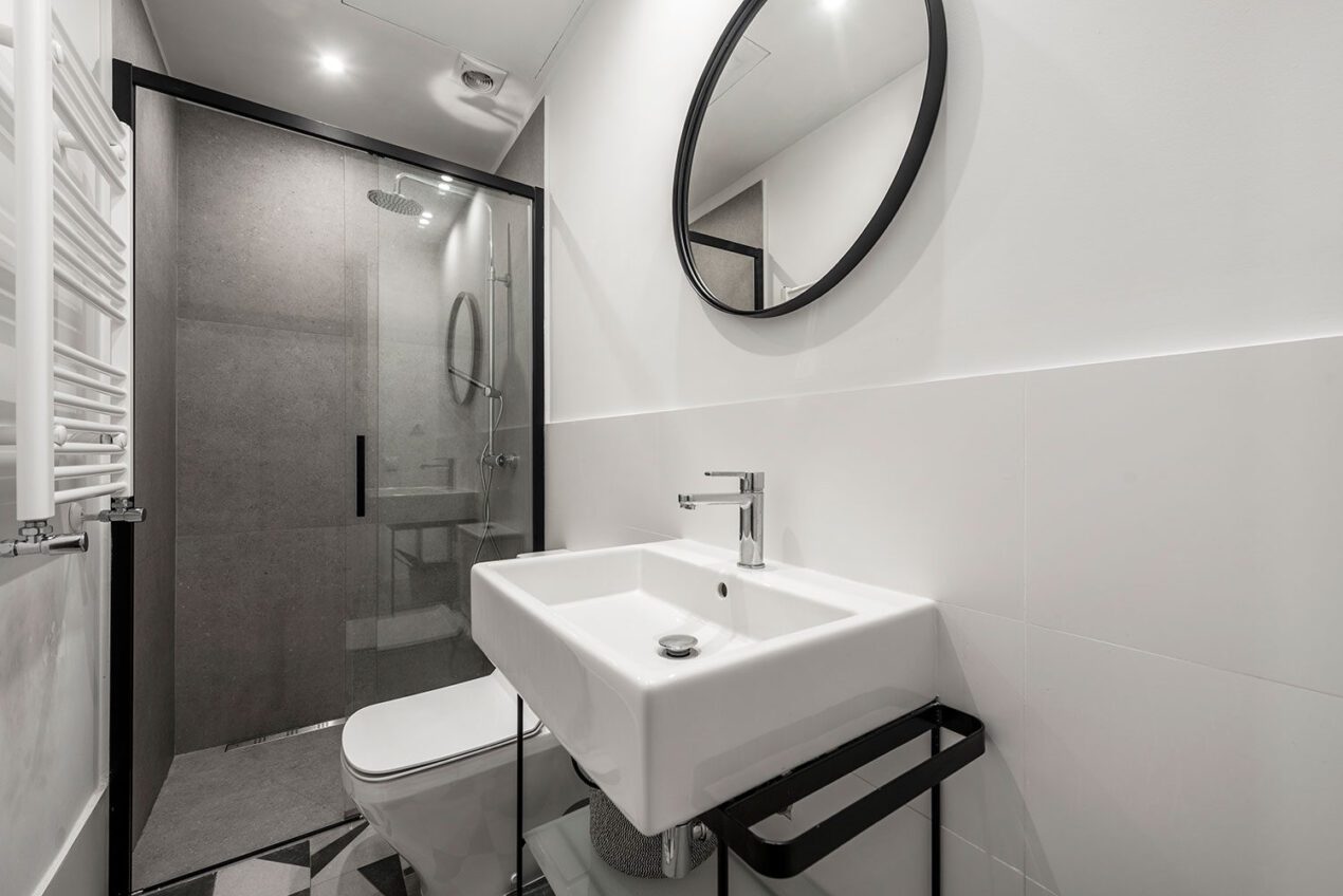 Modern small bathroom with black framed 2-panel sliding shower door and round mirror