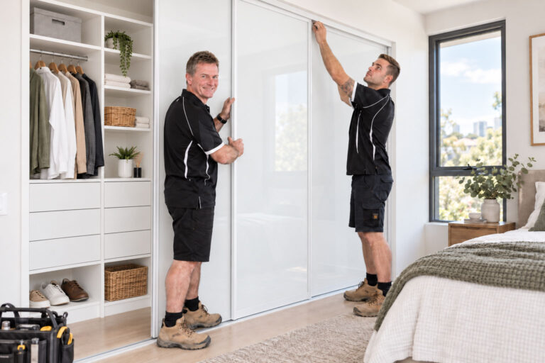 REGAL team installing white sliding wardrobe doors on a custom built-in wardrobe in a Brisbane bedroom